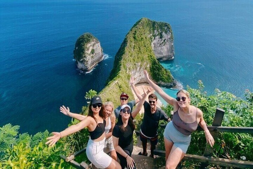 A group of people on a coastal trail with a view of a large rock formation and the ocean. 3