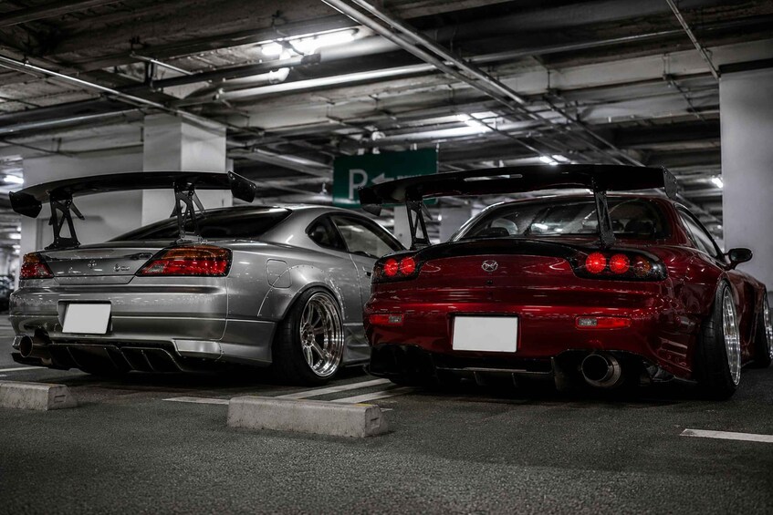 Two modified sports cars parked in a garage with visible exhaust pipes and rear spoilers. 2