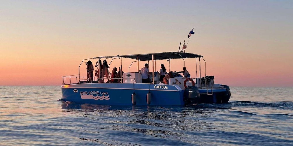 A boat with people on board, named 'MARINA YACHTING CEFALPI,' sailing on calm waters during sunset. 5
