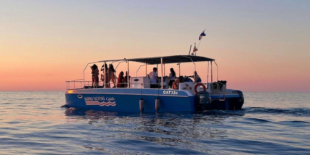 A boat named 'MARINA YACHTING CEFALPI' with passengers and a flag, sailing on calm waters during sunset. 3