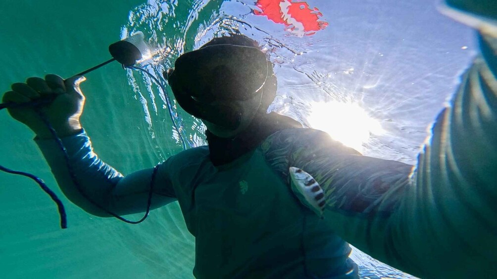 A person underwater, holding a flashlight, with sunlight reflecting off the water surface. 3