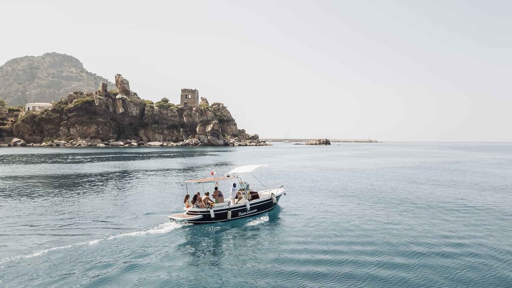 A boat named 'Dream Excursion' on calm waters with a rocky coastline and a castle-like structure in the background. 3