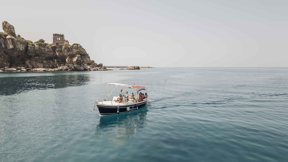 A boat with passengers on a calm sea, rocky cliffs, and a distant castle. 1