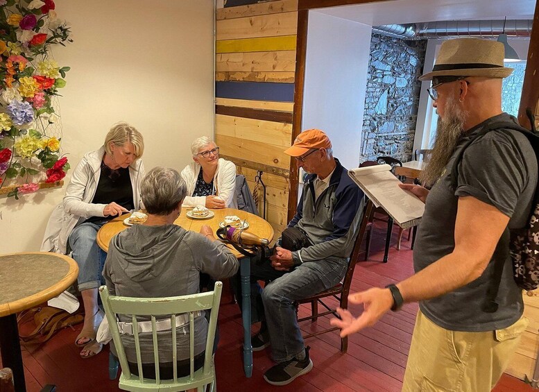 A group of people sitting around a wooden table with food, in a room with wooden walls and a floral decoration. 3
