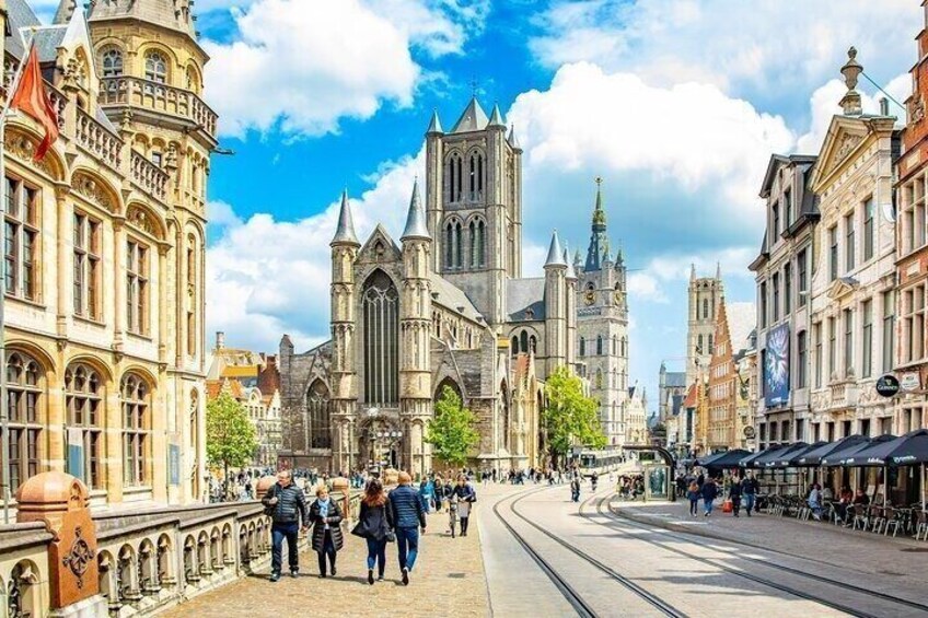 A historic city street with a prominent cathedral, tram tracks, and pedestrians. 1