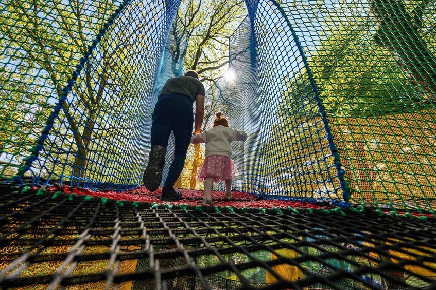 A person guiding a child through a netted obstacle course. 3