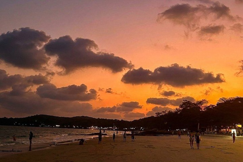 A beach at sunset with silhouettes of people and distant city lights. 3