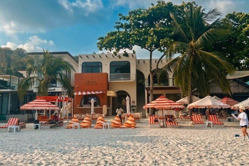 A beach with umbrellas, lounge chairs, and a building with a sign. 5