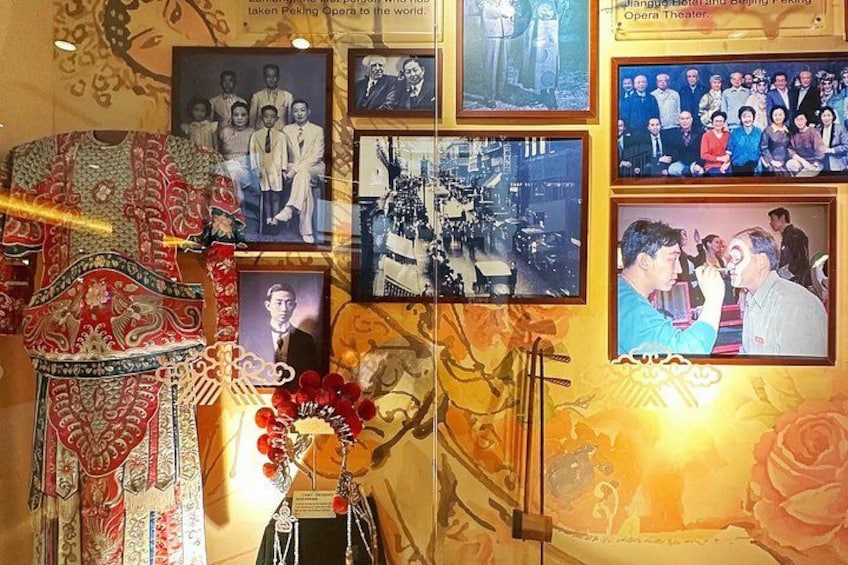 A wall with framed photographs, a traditional Chinese dress, and a vase with red flowers. 2