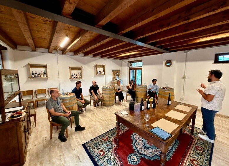 A group of people in a rustic room with wooden beams, barrels, and wine bottles. 2