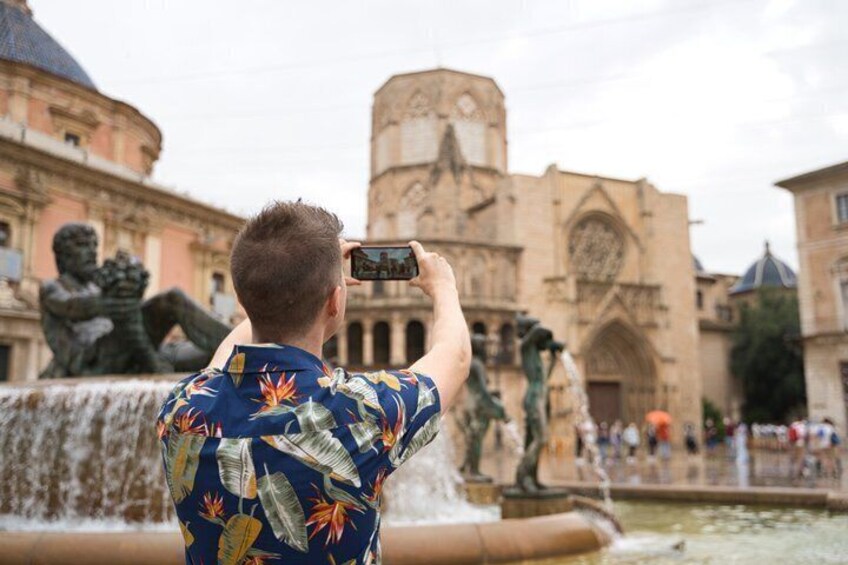 A person taking a photo of a historic building with statues and a fountain. 5