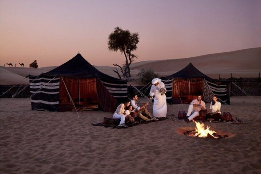 A desert camp with tents, a fire, and people sitting around. 1