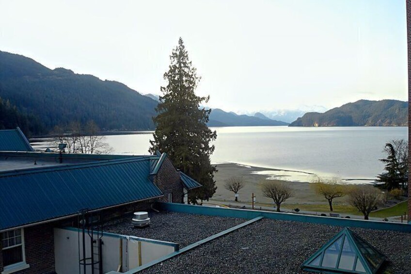 A building with a blue roof overlooking a calm lake with mountains in the background. 2