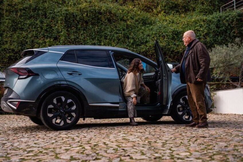 A blue SUV parked on a cobblestone surface with a man and a woman standing beside it. 5
