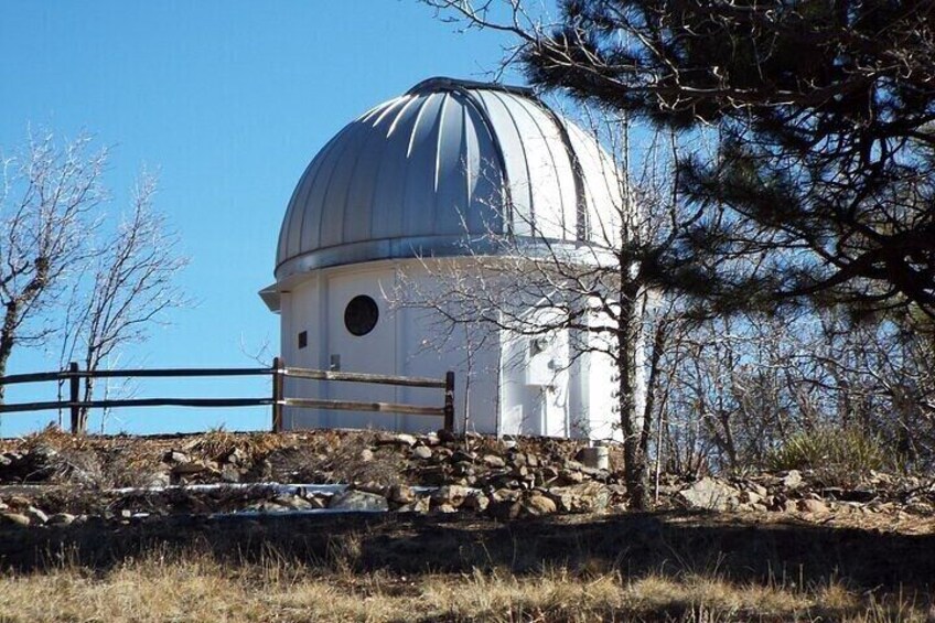 A domed observatory with a clear sky, surrounded by trees and a rocky landscape. 5