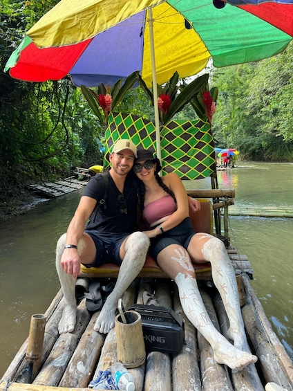 A couple on a bamboo raft with a colorful umbrella, surrounded by greenery and a river. 4