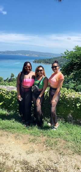 Three people standing on a grassy hill with a view of a coastline and hills in the background. 3