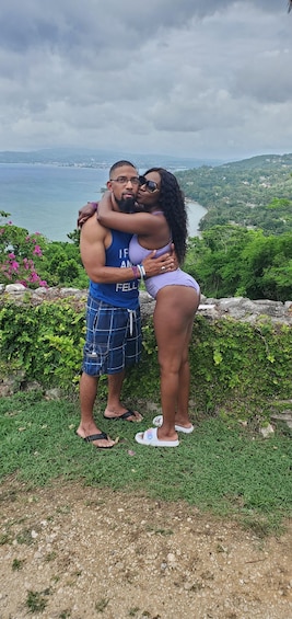 A couple embracing on a grassy hill with a river and mountains in the background. 2