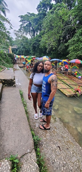 Two people standing by a river with a bridge and colorful umbrellas in the background. 1