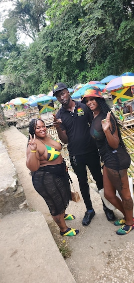 A group of people posing in a tropical setting with colorful umbrellas and a river in the background. 5