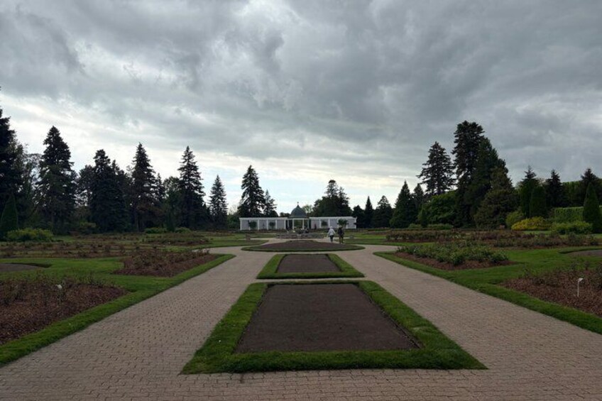 A formal garden with a central pathway, symmetrical flower beds, and a white building in the background. 3