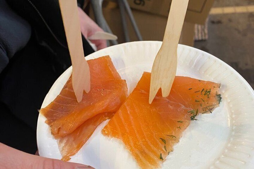 A plate with two pieces of smoked salmon on a white paper plate, garnished with dill. 1