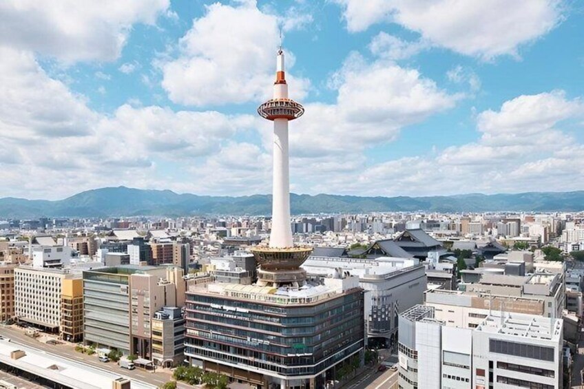 A cityscape with a prominent tower, modern buildings, and a distant mountain range. 1