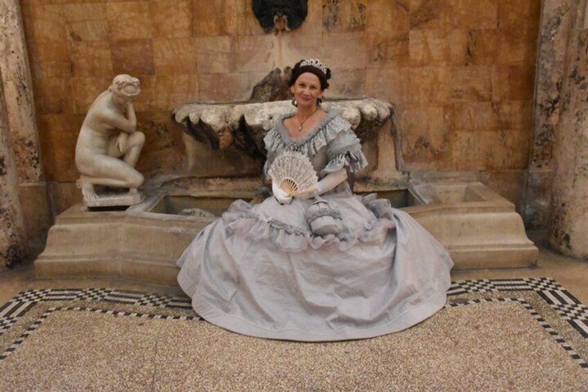 A person seated on a stone bench in a historical building with classical architecture, including a statue and a fountain. 1