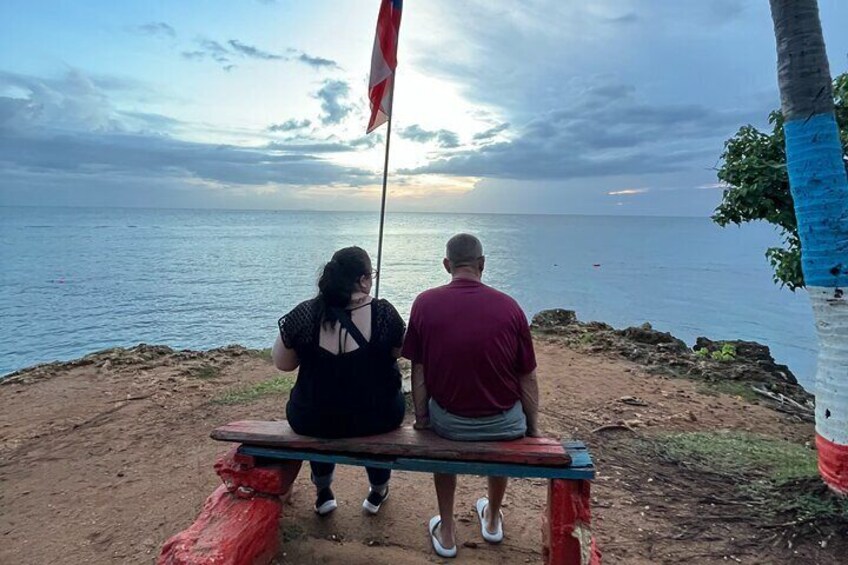 Two people sitting on a bench overlooking the sea with a flagpole in the background. 4