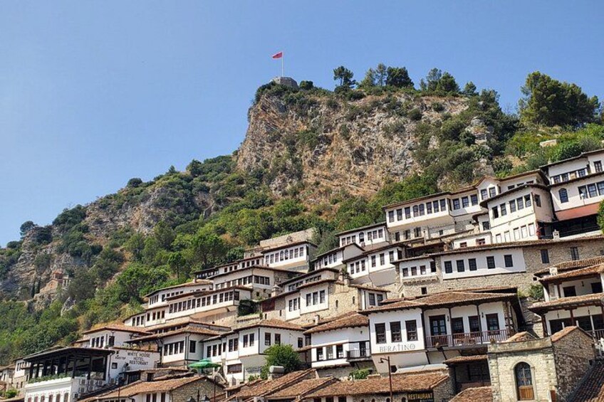 A hillside settlement with buildings, a flag, and a rocky mountain backdrop. 1