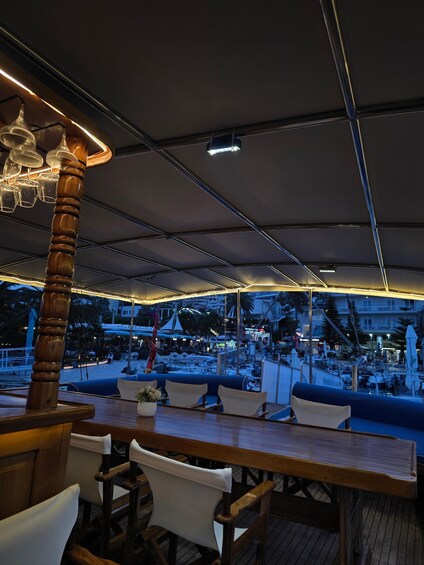 An outdoor restaurant with wooden furniture and a view of a busy harbor at dusk. 4