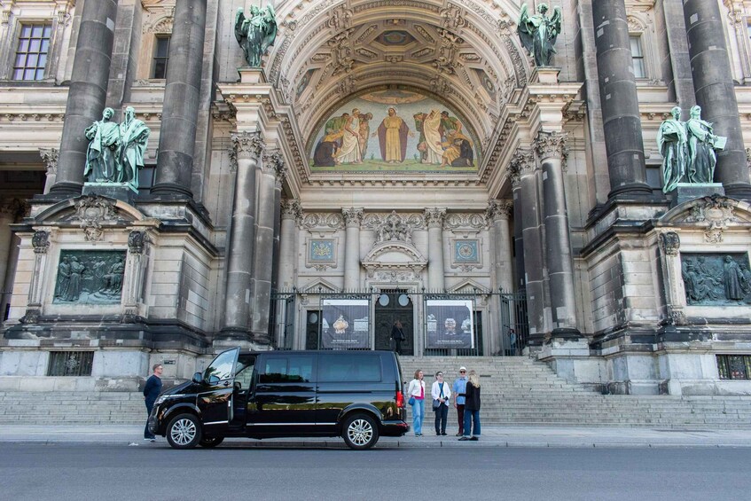A black SUV parked in front of a grand building with ornate columns and a detailed mosaic above the entrance. 3