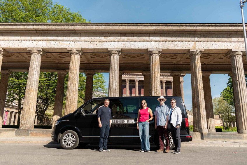 A black van parked in front of classical columns with people standing beside it. 4