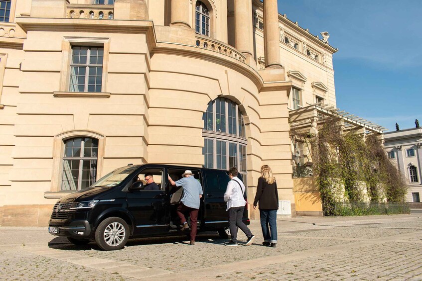 A black SUV parked in front of a classical building with columns and arched windows. 5