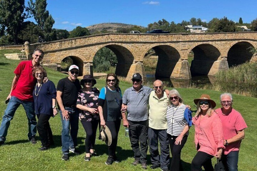 A group of people standing in front of a stone bridge with multiple arches. 1
