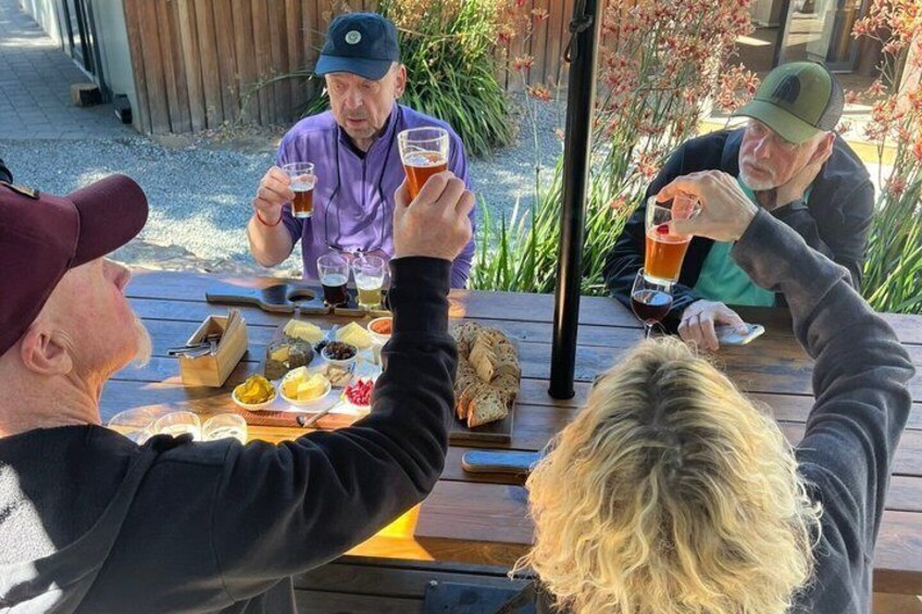 People sitting at a wooden table outdoors, holding glasses of beer. 4