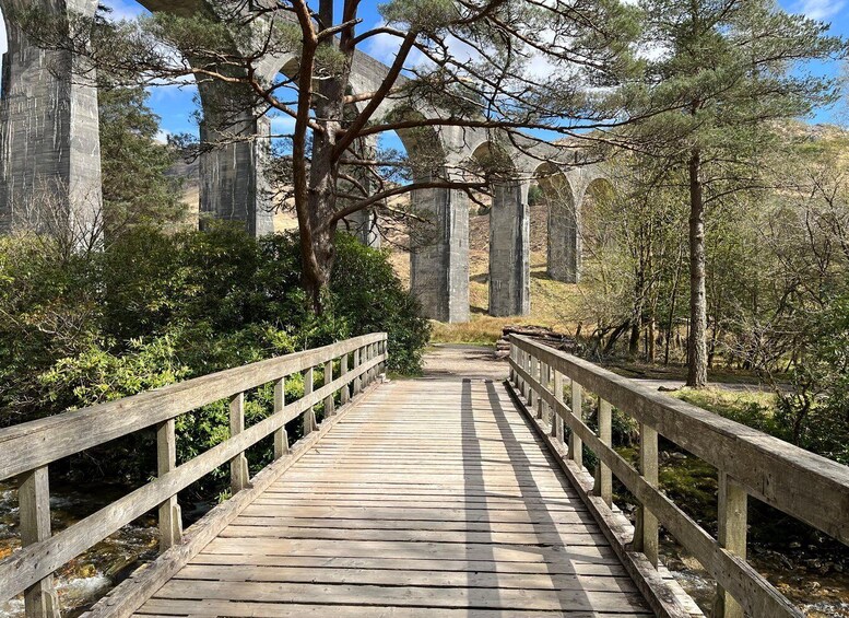 A wooden bridge with railings, surrounded by trees and stone arches in a natural setting. 2