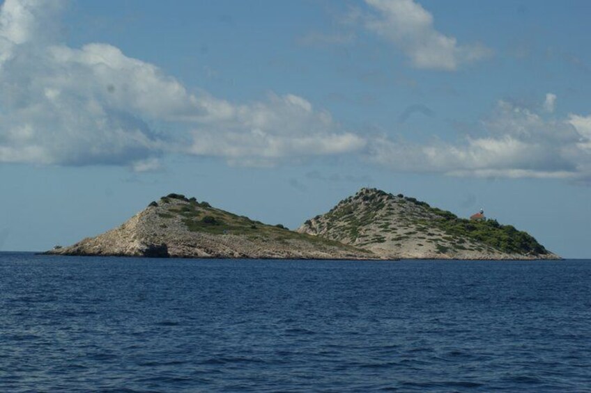 A small island with rocky terrain and sparse vegetation, surrounded by a calm sea under a partly cloudy sky. 5