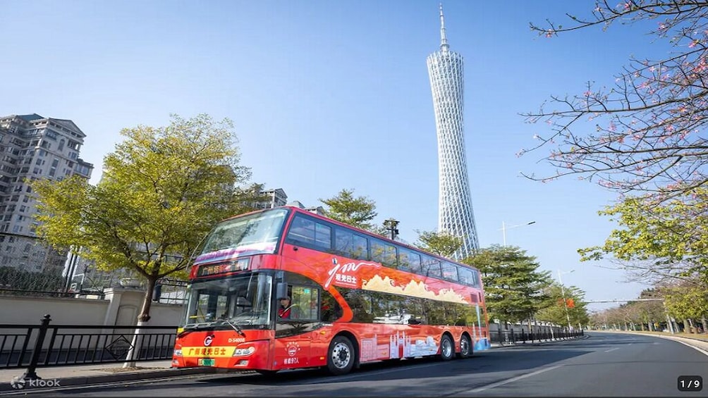 A red double-decker bus on a city street with a tall tower in the background. 5