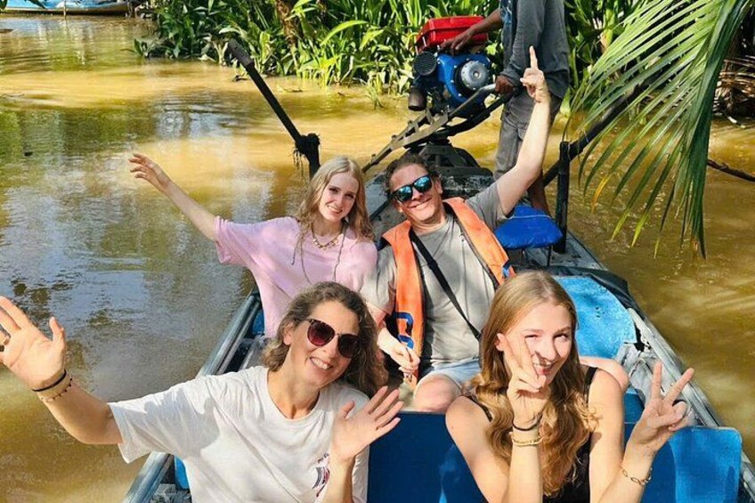 A group of people on a boat with water on the sides, surrounded by greenery. 1