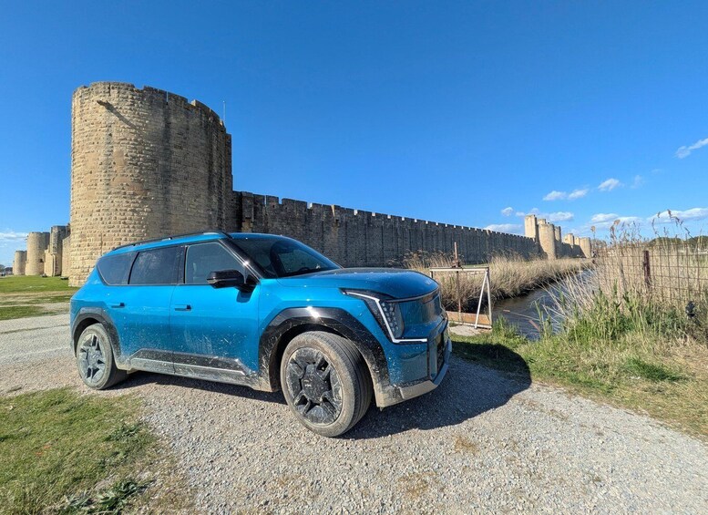 A blue SUV parked in front of a historic stone wall with a clear sky. 1