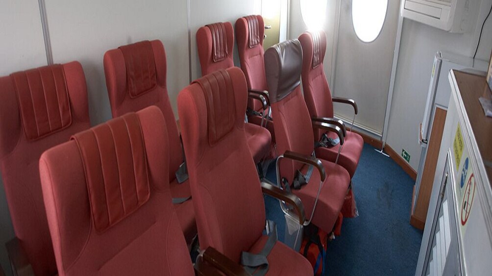 A row of red airplane seats with overhead compartments and a window. 2