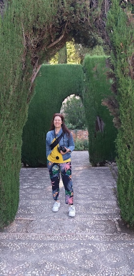 A person standing in a garden with a pathway, wearing a denim jacket, floral leggings, and holding a camera. 1