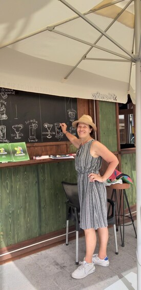 A person standing in front of a chalkboard with drink names and a wooden counter with cocktail boxes. 3