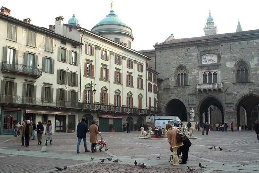 A historic square with pedestrians, pigeons, and classical architecture. 2