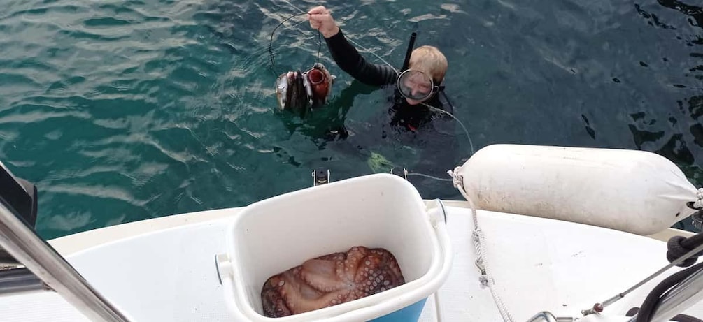 A person in a wetsuit holding a fish, a white container, and a buoy on a boat. 2
