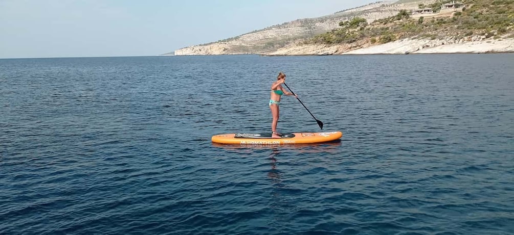 A person paddleboarding on a calm sea with a hilly coastline in the background. 3