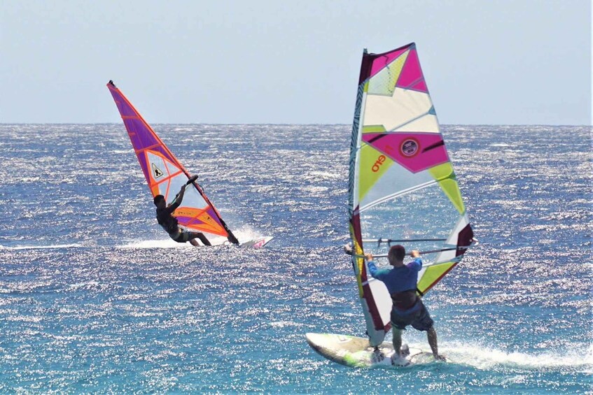 Two windsurfers on a clear day, one in the foreground and one in the background, both on a calm sea. 5