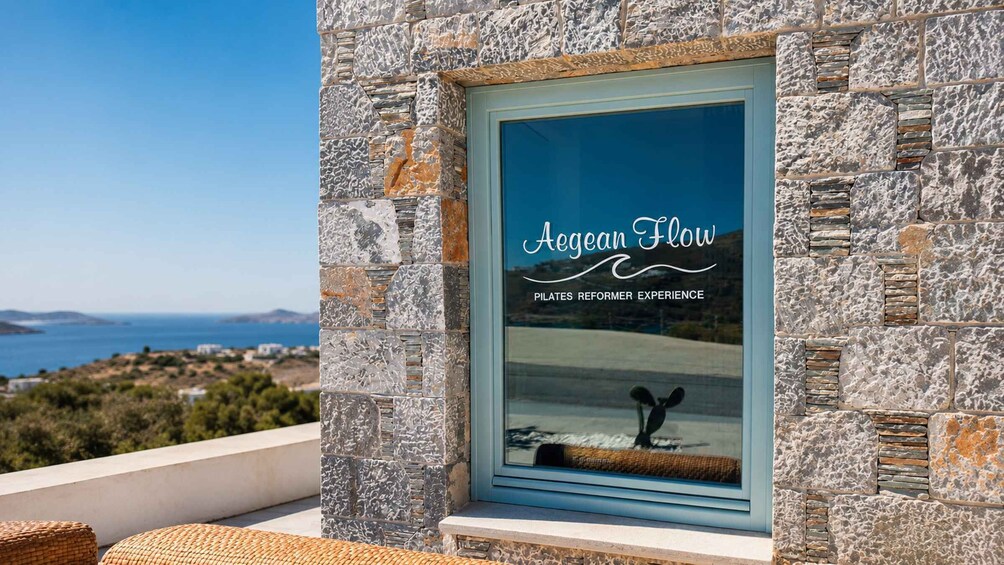 A stone wall with a window displaying 'Aegean Flow Pilates Reformer Experience.' 3