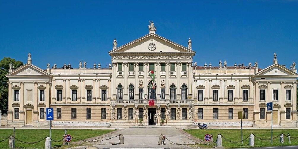 A classical building with a central entrance, statues, and a flag. 3